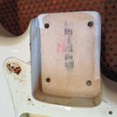 Detail zadní strany bílého kytarového trupu s vyfrézovaným výklenkem. V prostoru je vidět světlé dřevo s nápisem STD-5 a červeným znakem. Povrch bílé…