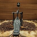 Černý dvojpedál na bicí s kovovou konstrukcí a stříbrnými detaily. Na plošince pedálu je vidět texturovaný povrch a bílý grafický symbol připomínajíc…