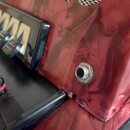 Detailní záběr na červený, lesklý povrch s mramorovým vzorem. Je vidět část klávesnice s bílými a černými klávesami a řada černých tlačítek. V červen…