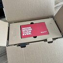 Fotografie ukazuje otevřený hnědý kartonové krabice, ve které je umístěno červené obalové etui. Na etui je bílý nápis MORE SPARK THAN EVER. a vpravo…