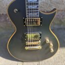 Černá elektrická kytara s gold hardwarem a hnědým lemováním kolem korpusu. Nástroj má dva humbuckery, Tune-o-matic můstek a tři zlaté ovládací knoflí…
