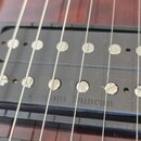 Detailní pohled na dva černý humbuckery s kovovými póly umístěné v černém rámečku na dřevěném hředu kytary. Na spodním snímači je vyražen nápis Seymo…