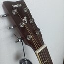 Hlava hnědé akustické kytary se značkou YAMAHA a bílým logem v podobě stylizovaného symbolu. Nástroj má stříbrné ladičky a bílou matku. K hlavě je př…