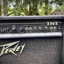 Černý kytarový kombozesilovač s nápisem TNT v pravém horním rohu a velkým logem Peavey na předním textilním krytu. Ovládací panel obsahuje řadu posuv…