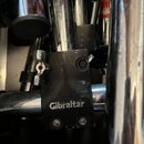 Detailní záběr na černý kovový spojovací prvek značky Gibraltar, který spojuje dvě chromované trubice. Na černé části je bílý nápis Gibraltar. Povrch…