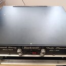 Černý rackový lambda zesilovač s kovovým šasi. Na předním panelu jsou nápisy Rockwell, POWERING SOUND, Tube Power Amplif, 50/50 a EL-34. Zařízení má…