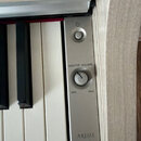 Detailní pohled na ovládací panel digitálního pianina v stříbrné barvě. Panel obsahuje tlačítko napájení, otočný ovladač s nápisy MASTER VOLUME, MIN…