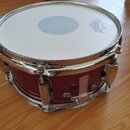 Červený snare drum s chromovaným obručováním a mechanismem. Na bílém koženu je vidět logo REMO s nápisem COATED AMBASSADOR. Nástroj vykazuje známky p…