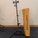 Kovový stojan s černými nohami a stříbrným teleskopickým trubkovým tělem. Vedle stojanu stojí kartonová krabice s nápisy BONGO STAND a MADE IN THAILA…
