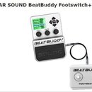 Bílá elektronická doprovodná bicí BeatBuddy a připojený bílý pedál Footswitch. Na hlavním zařízení je displej s textem Smooth Blues, Genre: Jazz, Tem…