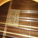 Detail vnitřku akustické kytary s viditelnými žebry a strunami. Uvnitř korpusu je nalepený bílý štítek s textem: MODEL G7-12, The LOWDEN guitar is ha…