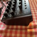 Černý elektronický syntetizátor s mnoha ovládacími knoflíky a přepínači. Na horním panelu je bílé logo behringer a nápis MIDI IN u kruhového konektor…