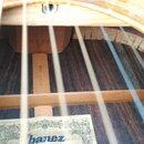 Detailní pohled do dutiny akustické kytary. Na vnitřní dřevěné liště je svisle napsán kód N0011516 a v horní části jsou vidět znaky 02 14 K. V dolní…