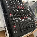 Černý DJ mixér umístěný v transportním kufru. Na levém boku je svisle napsáno "M DJ" a "Pioneer DJ". Přístroj obsahuje řadu červených a černých ovále…