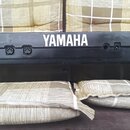 Černý plastový kufr s bílým nápisem YAMAHA. Na přední straně jsou vidět dva zámky a dvě otvory pro upevnění. Povrch plastu vykazuje drobné škrábance…