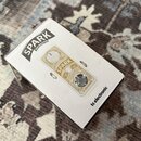 Bílá krabička s obrázkem efekt pedálu. Na krabici je nápis SPARK MINI BOOSTER a v pravém dolním rohu značka tc electronic. Zobrazený pedál je béžové…