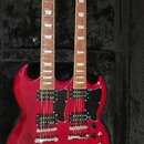 Dvě červené elektrické kytary typu SG v černém tvrdém kufru. Na hlavách je nápis Harley Benton a logo HB. Instrumenty mají dva humbuckery, černé plec…