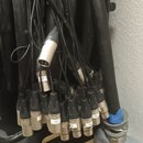 Sada černých audio kabelů s konektory XLR v kovovém provedení. Některé konektory mají bílé papírové štítky s ručně psanými označením, například 3, 2P…
