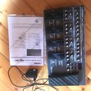 Na dřevěné podlaze leží multifunkční efektový procesor Boss ME-80 v černé barvě s ovládacími knoflíky a pedály. Na zařízení je vidět nápis BOSS ME-80…