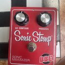 Červený kytarový efekt s nápisy LO CONTOUR a PROCESS u dvou černých ovládacích knoflíků. Uprostřed je velký bílý nápis Sonic Stomp a v dolní části te…