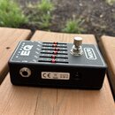 Černý kytarový ekvalizér s nápisy SIX BAND EQ a MXR. Zařízení má šest posuvníků s červenými knoflíky, stříbrný zapínací spínač a konektory OUT a napá…