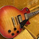 Elektrická kytara typu Les Paul v červeno-žlutém sunburst provedení s viditnou strukturou dřeva. Nástroj má dva humbuckery, čtyři černé oválné knofík…