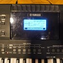 Černý digitální klavír s logem YAMAHA nad displejem. Podsvícený displej zobrazuje nápis GrandPno, hodnotu 001 a další nečitelné údaje. Povrch plastov…