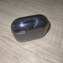 Černý nabíjecí box s průhledným víkem, uvnitř kterého jsou umístěna dvě bezdrátová sluchátka. Na horní části víka je bílý nápis SAMSUNG. Povrch průhl…