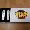 Bílá krabice s žlutým logem LACE MUSIC PRODUCTS obsahuje dva bílé snímače s kulatými póly. Snímače jsou umístěny v černém vložném materiálu. Povrch k…