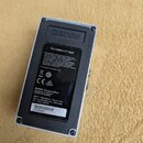 Zadní strana šedého efektpedálu s černým plastovým krytem baterie. Na štítku je nápis Dry battery 9 V type, značka BOSS Corporation a text Products o…