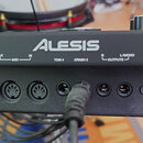 Černý elektronický modul značky ALESIS s řadou konektorů na předním panelu. Jsou zde nápisy USB MIDI, OUT MIDI IN, TOM 4, CRASH 2, R L/MONO OUTPUTS,…