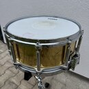 Zlatý buben s bílým membránou, který stojí na chromovaném stojanu. Na horní membráně je viditelný nápis EVANS a světle růžový samolep. Korpus má chro…