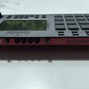 Černý sampler s červeným spodním rámem. Na zadní straně je nápis AKAI PROFESSIONAL MPC a řada konektorů s popisky POWER, DC IN, USB, VOL, IN, OUT, PH…