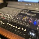 Černý mixovací pult s velkým množstvím posuvníků, knoflíků a tlačítek. Na pravé straně jsou vidět nápisy HERITAGE EDITION, MIX PROCESSING a TALKBACK.…