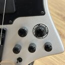 Detail stříbrného trupu elektrické kytary s černým pickguardem. Na povrchu jsou umístěny čtyři černé oválné knofíky a jeden větší černý knofík s bílý…