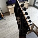 Černá hlava elektrické kytary s šesti ladicími kolíky. Na povrchu je viditelné zlaté logo "ESP". Lak na hraně hlavy vykazuje drobné odřesy a opotřebe…