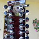 Detail hlavy kytary z tmavého dřeva s lakovaným povrchem. V horní části je bílý nápis Canglonwood Guitar Company UNITED KINGDOM. Na hlavě jsou instal…