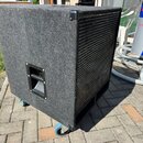 Štíhlý basový reproduktor v černém plátnovém potahu s kovovou mřížkou na přední straně. Na boku je umístena černá plastová rukojeť a v dolní části js…