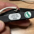 Detailní pohled na zadní stranu černé snímače s připojenými bílým a červeným vodičem. Na povrchu je bílá oválná nálepka s nápisem NECK PICK UPS BHK a…