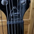 Detail hlavy černé elektrické kytary s viditelným logem Framus. Pod ním jsou nápisy SERIES a IDOLMAKER. Povrch laku je v horní části mírně znečištěný…