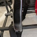 Detailní pohled na hranu hlavy kytary v černé barvě s viditnou strukturou dřeva. Na levé straně jsou vidět čtyři černé ladicí mechanismy. Povrch lako…