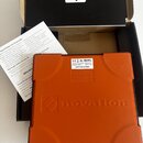 Oranžový MIDI kontrolér Novation Launchpad Mini v originální krabici. Na horní straně je nápis novation a logo značky, na spodní straně štítky s nápi…