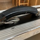 Detailní pohled na úchytku černého transportního kufru s hliníkovým profilem. Samotná rukojeť je omotaná černou izolační páskou, která vykazuje známk…