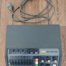 Šedý rytmus stroj s nápisem KORG RHYTHM 55B. Horní panel obsahuje pět otočných potenciometrů pro ovládání hlasitosti jednotlivých nástrojů a řadu bar…