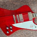 Červená elektrická kytara s dumpedým tvarem těla a bílým plechtrákem. Na plechtráku je viditelné logo s ptačím motivem a nápisem Epiphone. Nástroj má…