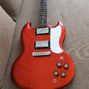 Elektrická kytara s červeným kovovým lakem a bílým pickguardem. Nástroj má dva humbuckery, stříbrný most a čtyři černé ovládací knoflíky. Na hlavě hm…