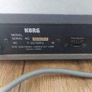 Detail zadní strany šedého elektronického přístroje se štítkem značky KORG. Na štítku je uveden nápis MODEL KR-50B, SERIAL NO. 394093 a údaje AC 220…