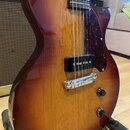 Detail elektrické kytary s trupem v červenohnatém sunburst provedení a viditelnou strukturou dřeva. Nástroj má tmavý hmatník, černý snímač a tmavě če…