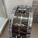 Detailní pohled na bok černého bubnu s chromovaným kováním. Na korpusu je vidět nápis "Slingerland". Povrch je lesklý, kování vykazuje známky běžného…