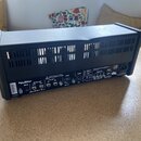 Zadní strana černého kytarového komba s plastovým krytem. Na zadním panelu jsou vidět nápisy „Hughes & Kettner“, „MIDI IN“, „FOOTSWITCHES Channels /…